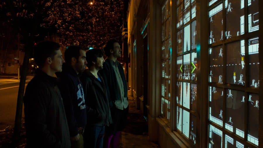 The artists and engineers responsible for creating the CTRL ALT PDX game standing in a line in front of the game with light from the game reflecting across their faces